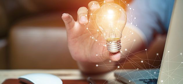 A person is holding a light bulb in their hand in front of a laptop.