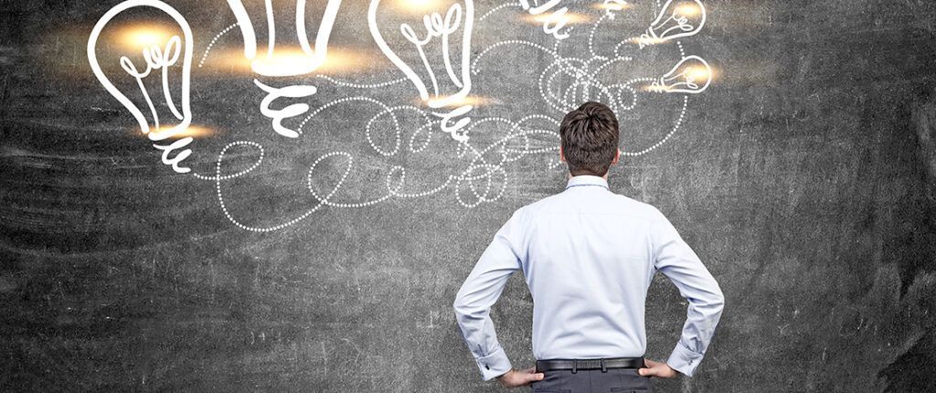 A man is standing in front of a blackboard with light bulbs drawn on it.