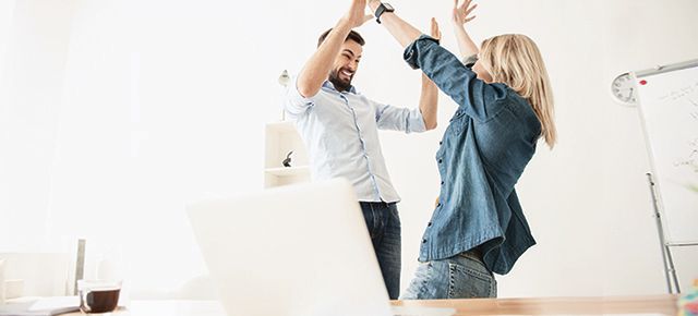 A man and a woman are giving each other a high five in an office.
