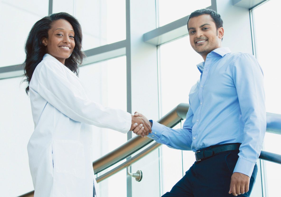 A man and a woman are shaking hands in front of a window.