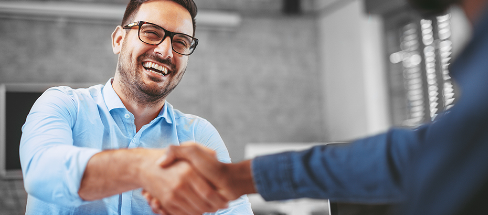 Two men are shaking hands in an office and smiling.