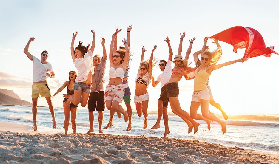 A group of people are jumping in the air on the beach.