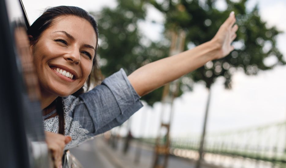 A woman is smiling and waving out of a car window.