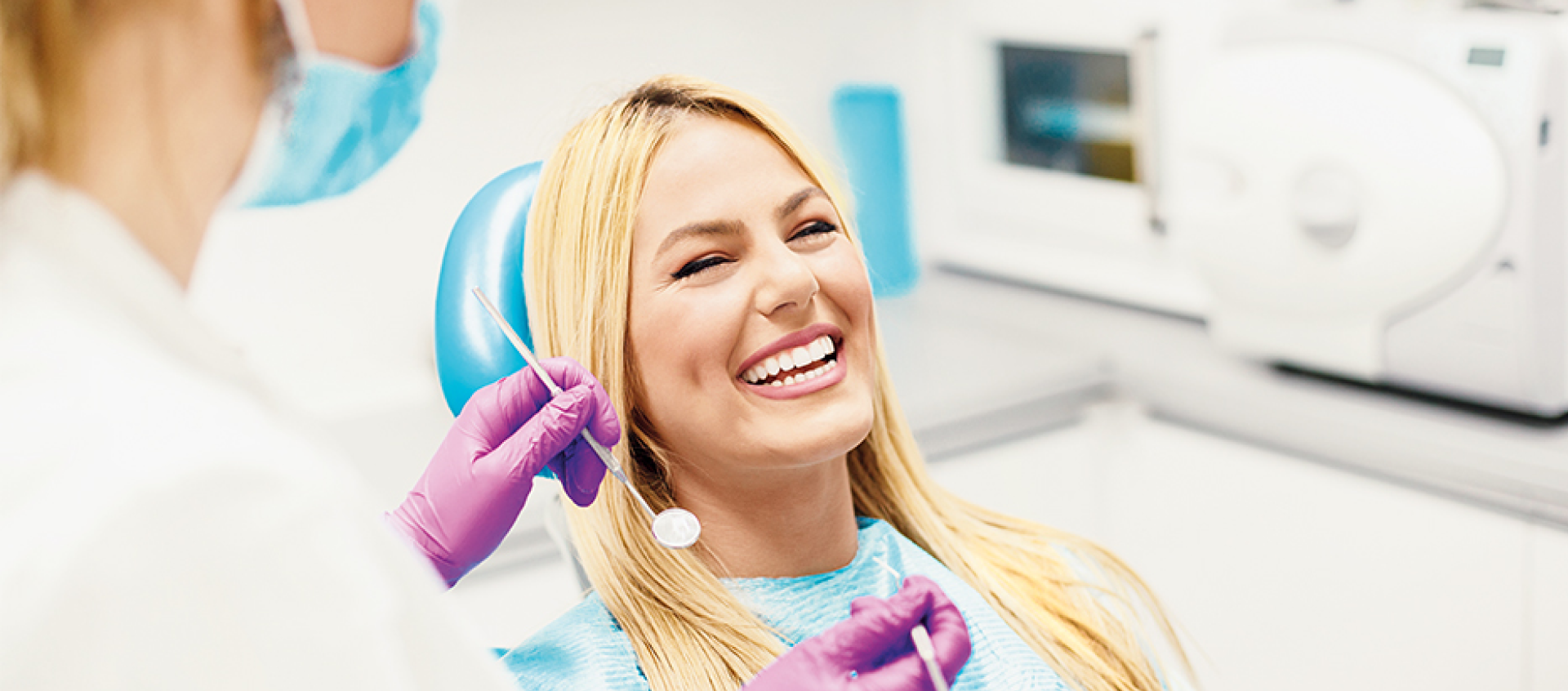 A woman is smiling while sitting in a dental chair.