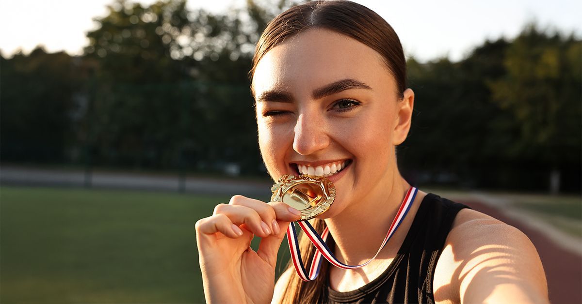 Athlete smiling and biting a gold medal on a track field.