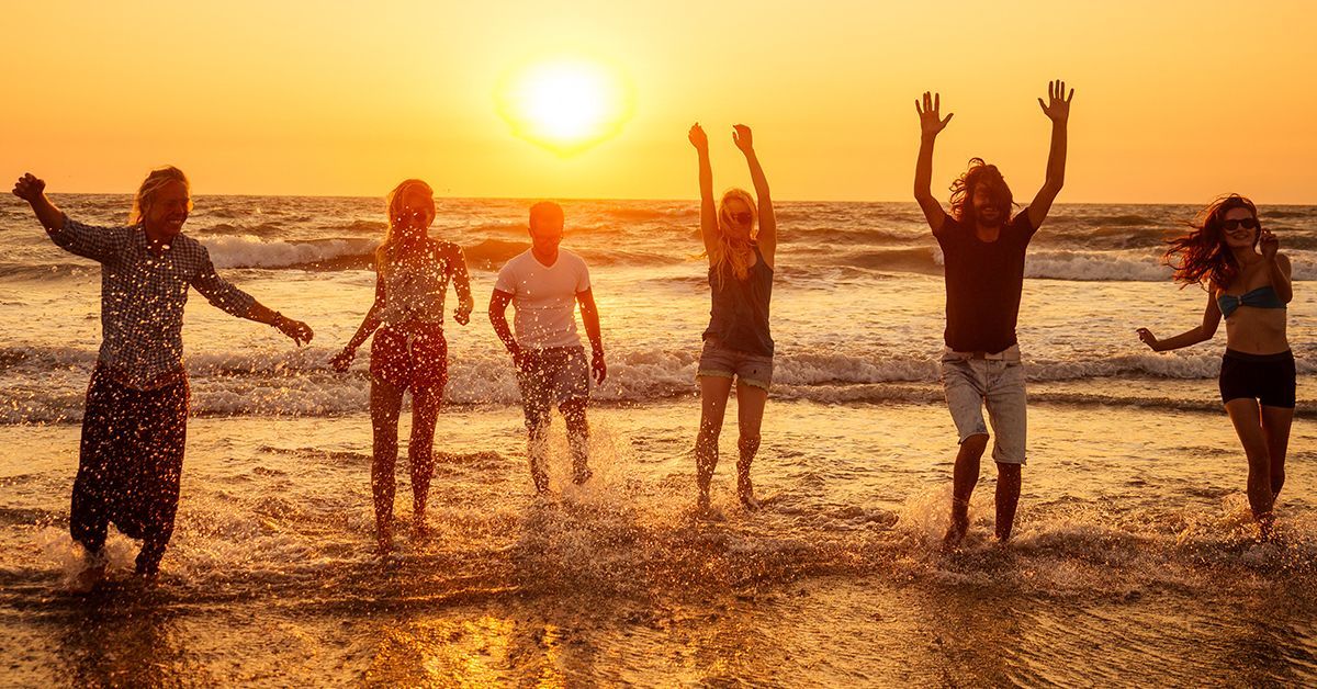 Group of friends running and splashing in the ocean at sunset.