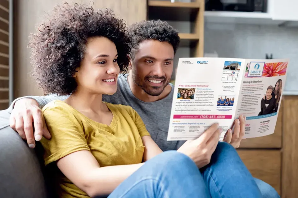 Couple sitting on a couch reading a Dental brochure together at home.