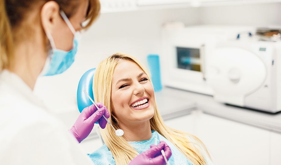 A woman is smiling while sitting in a dental chair.