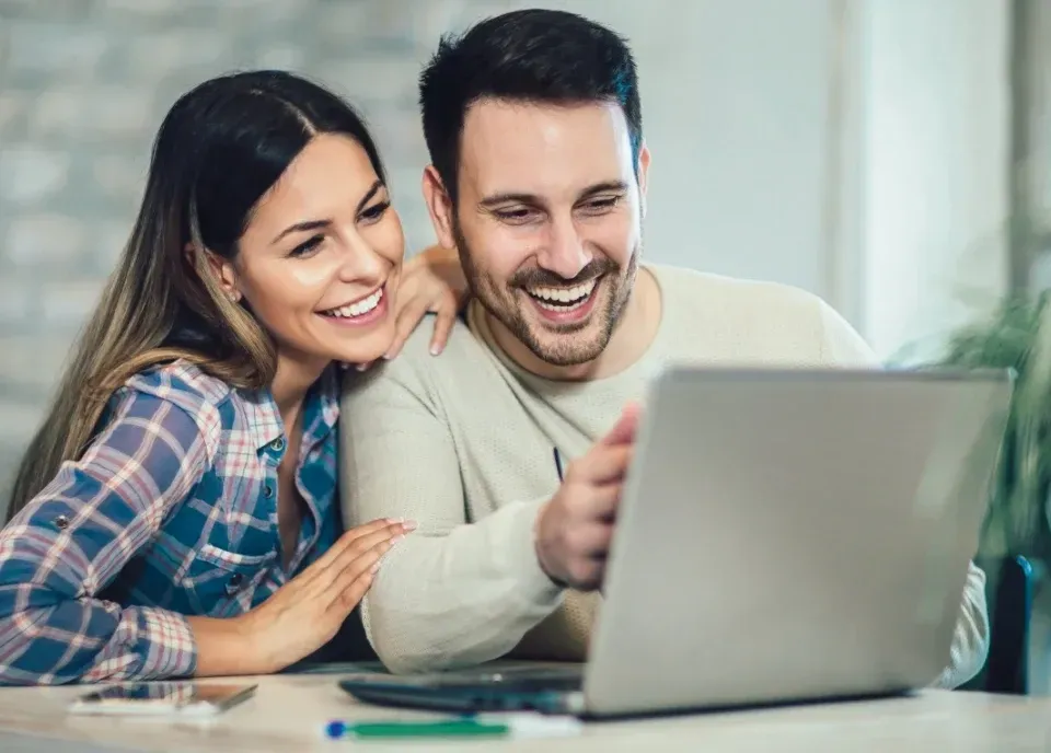 Couple smiling while using a laptop at home.