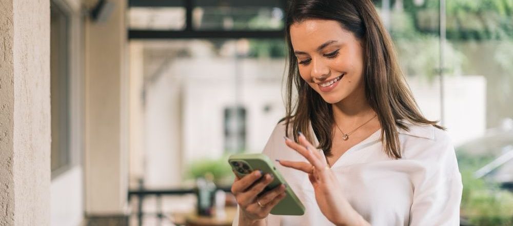 A woman is smiling while looking at her cell phone.