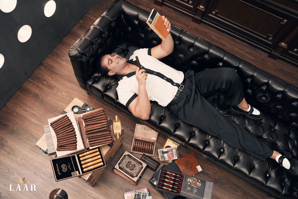 Person lying on a black leather couch beside books, wearing a white shirt and black suspenders