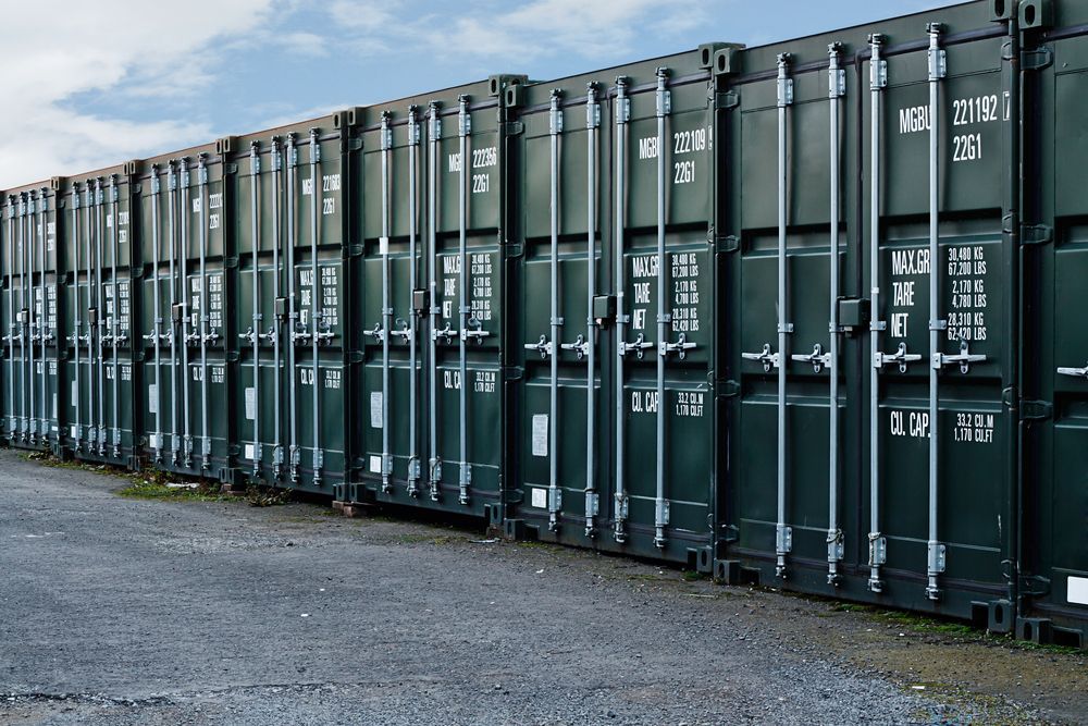 Row of dark green shipping containers along a gravel lot under a cloudy sky — All Sunshine Coast Towing In Sippy Downs, QLD