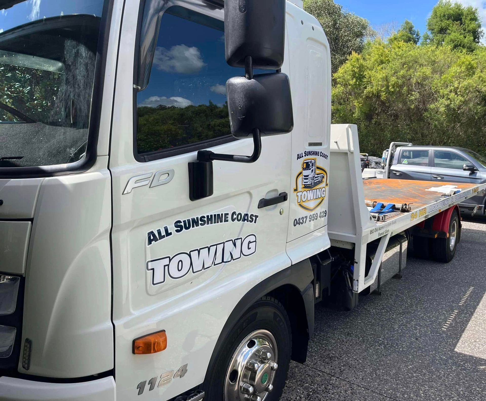 Tow truck carrying a car on a road, with a white cab and flatbed under sunny skies  — All Sunshine Coast Towing In Forest Glen, QLD