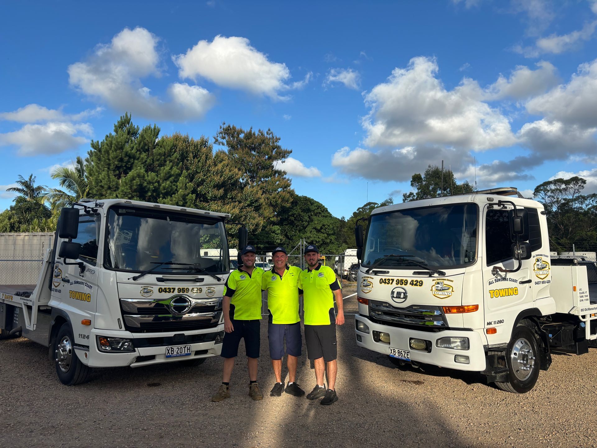 Four people in neon shirts standing between two white trucks on a sunny day — All Sunshine Coast Towing In Maroochydore, QLD