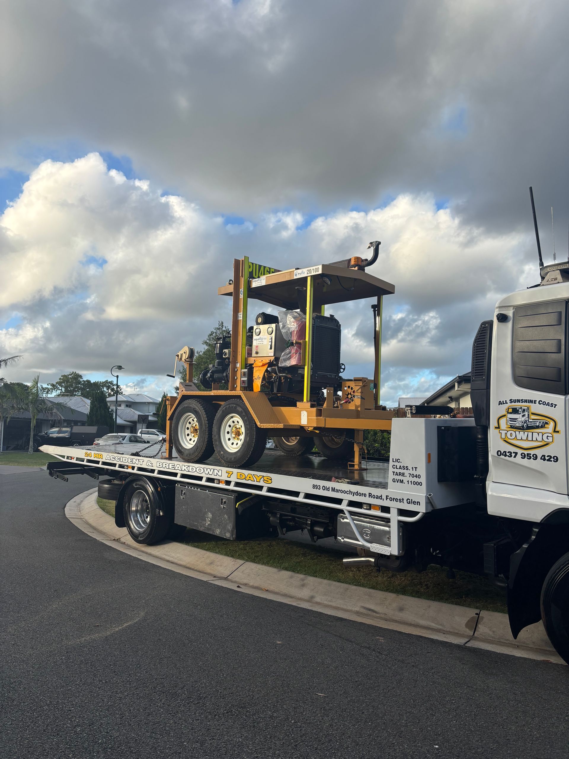 Flatbed truck carrying a yellow forklift on a road under cloudy skies — All Sunshine Coast Towing In Forest Glen, QLD