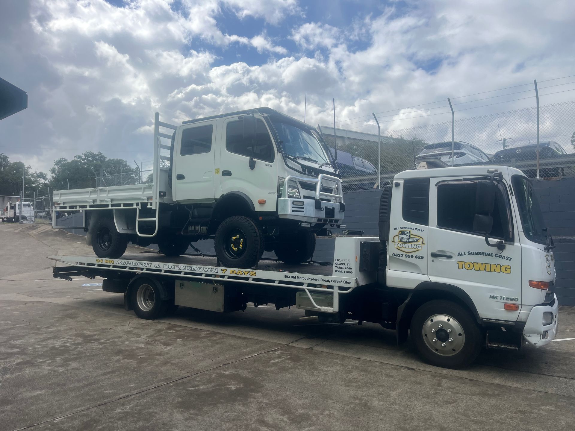 White tow truck hauling a white flatbed truck in a muddy lot under a cloudy sky — All Sunshine Coast Towing In Sippy Downs, QLD