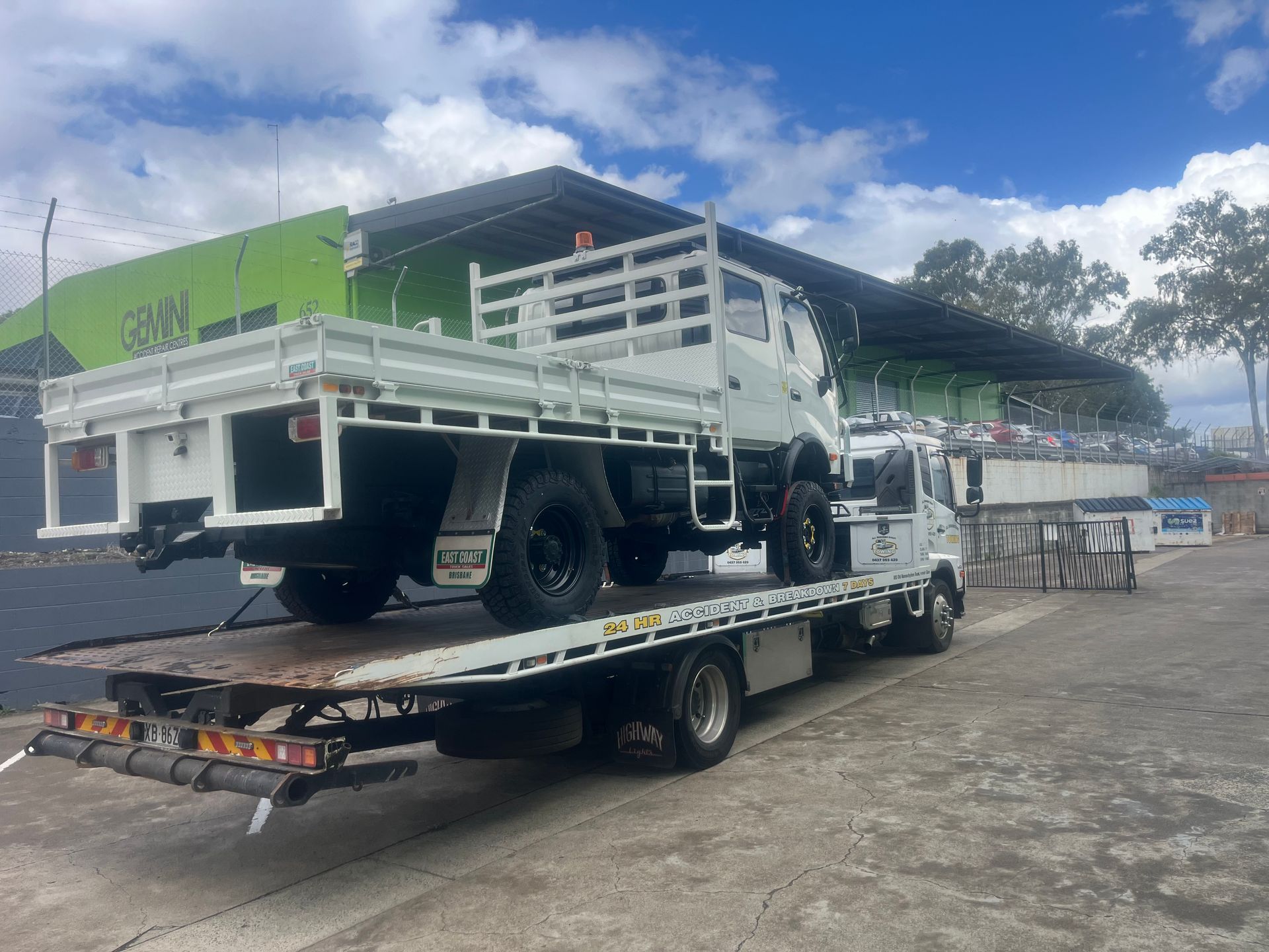 Flatbed trailer carrying a white utility truck in a gravel lot under a cloudy sky — All Sunshine Coast Towing In Maroochydore, QLD