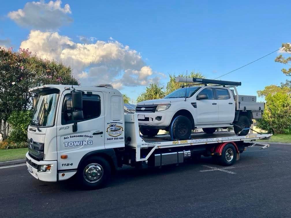 Tow truck carrying a white pickup truck on a flatbed, parked on a road under a blue sky. — All Sunshine Coast Towing In Forest Glen, QLD