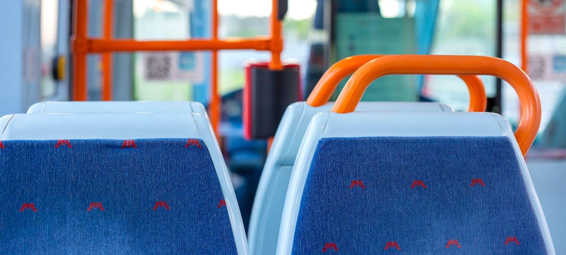 Nahaufnahme von blau gemusterten Sitzen mit orangefarbenen Haltegriffen im Inneren eines Busses.