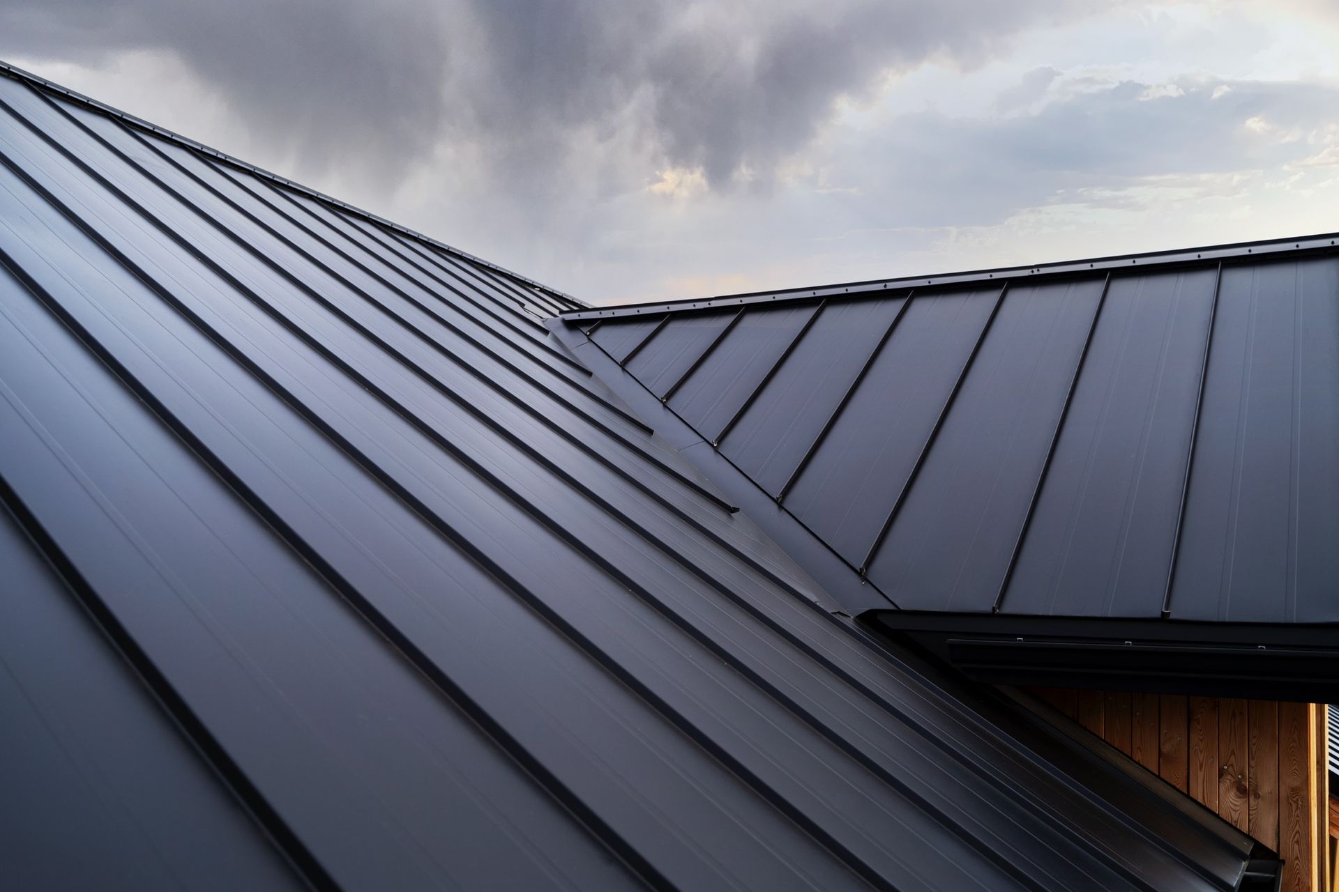 Dunkelgraues Stehfalzdach aus Metall vor bewölktem Himmel.