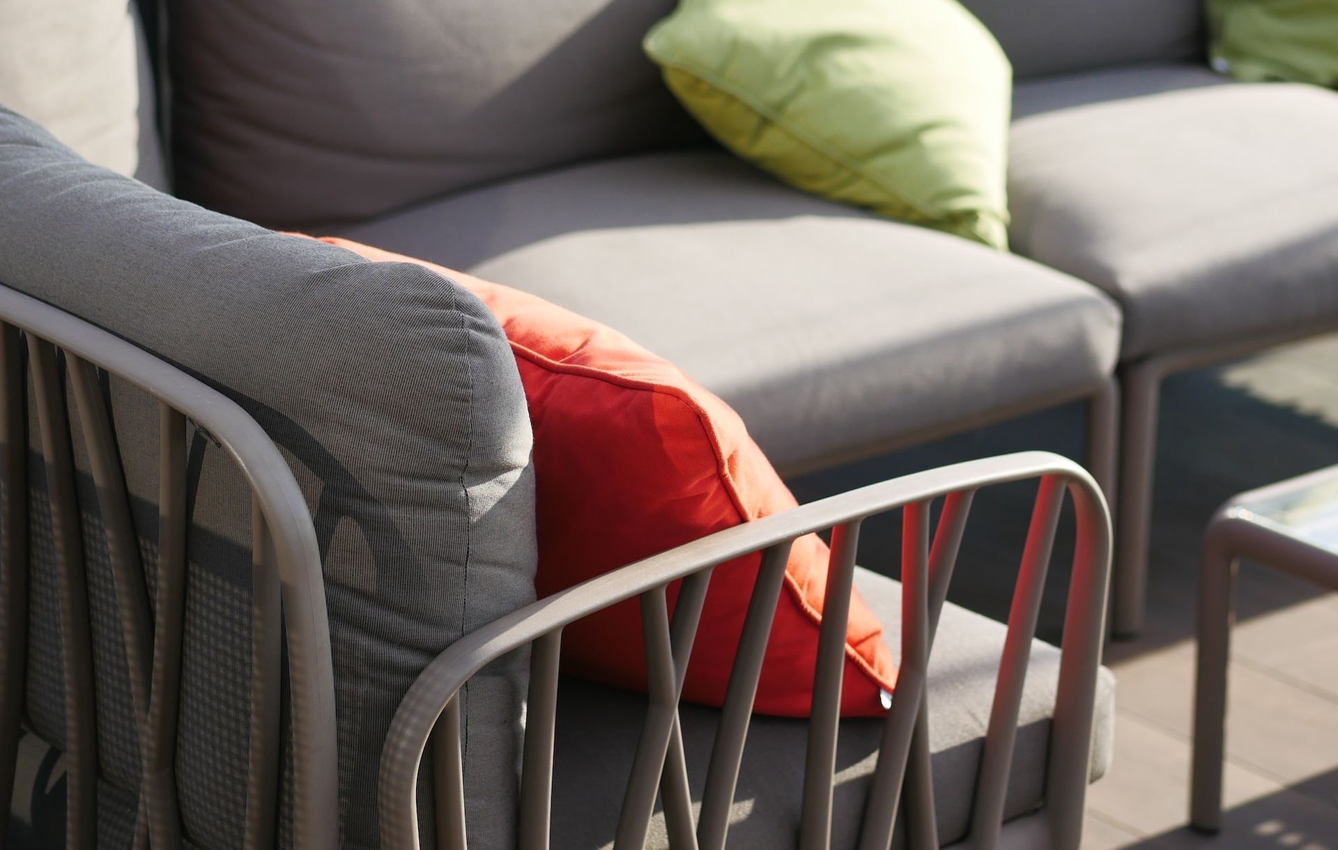 Gartenmöbel für die Terrasse mit grauen Kissen und orangefarbenen und grünen Zierkissen, die über ein dekoratives, gewebtes Metallgestell verfügen.