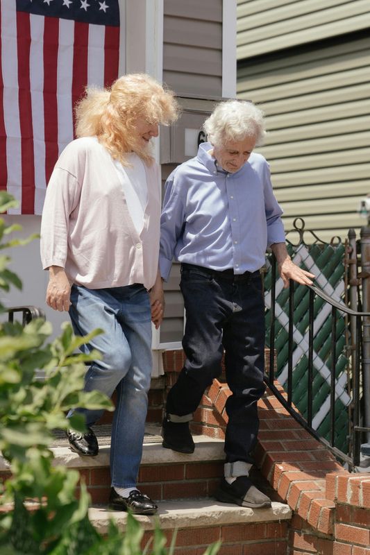 Two people descend steps from a house; American flag on the wall.