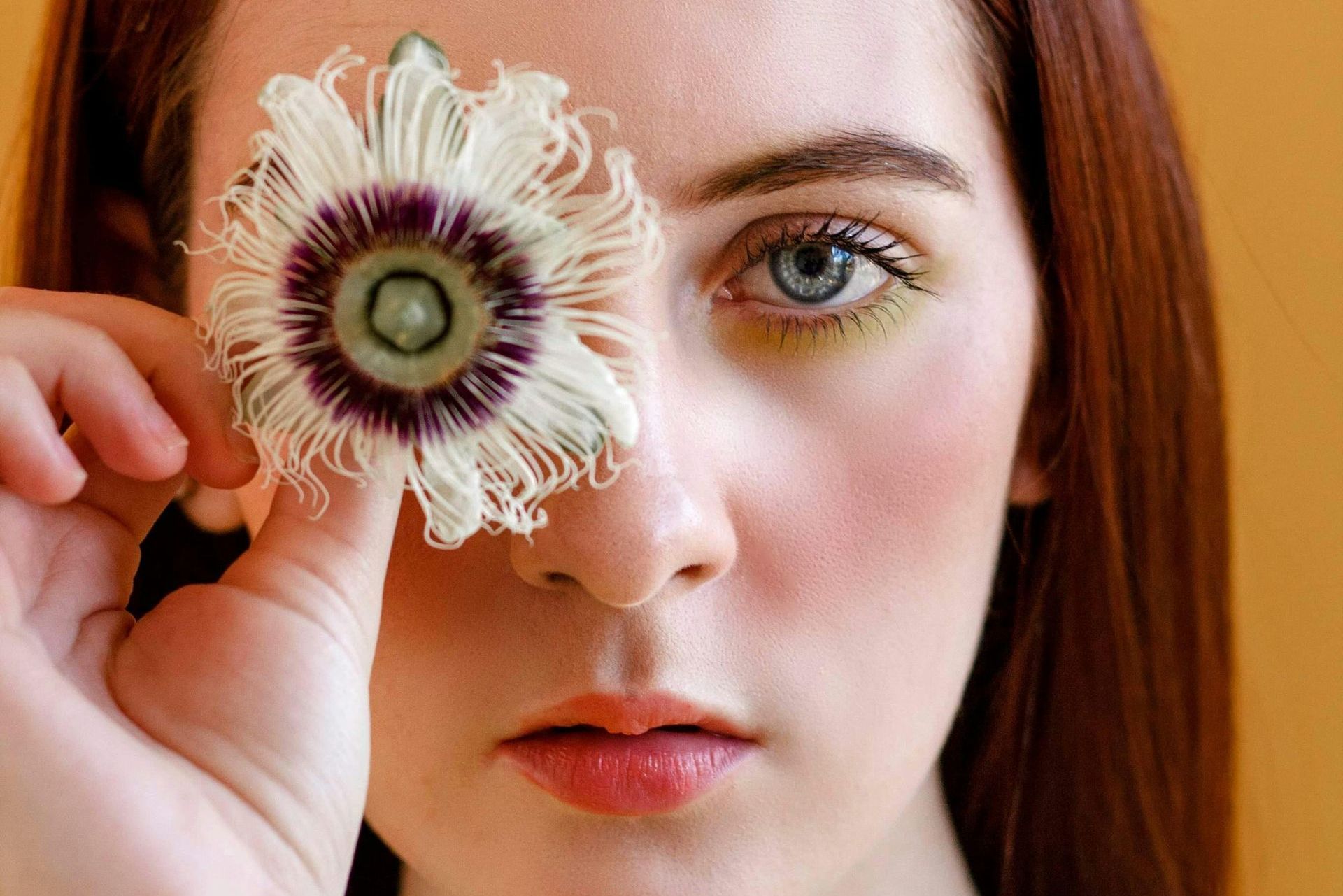 Junge Frau verdeckt ein Auge mit einer Blüte