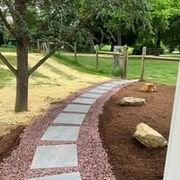 Curved stone path through a lush green garden beside white houses on a sunny day
