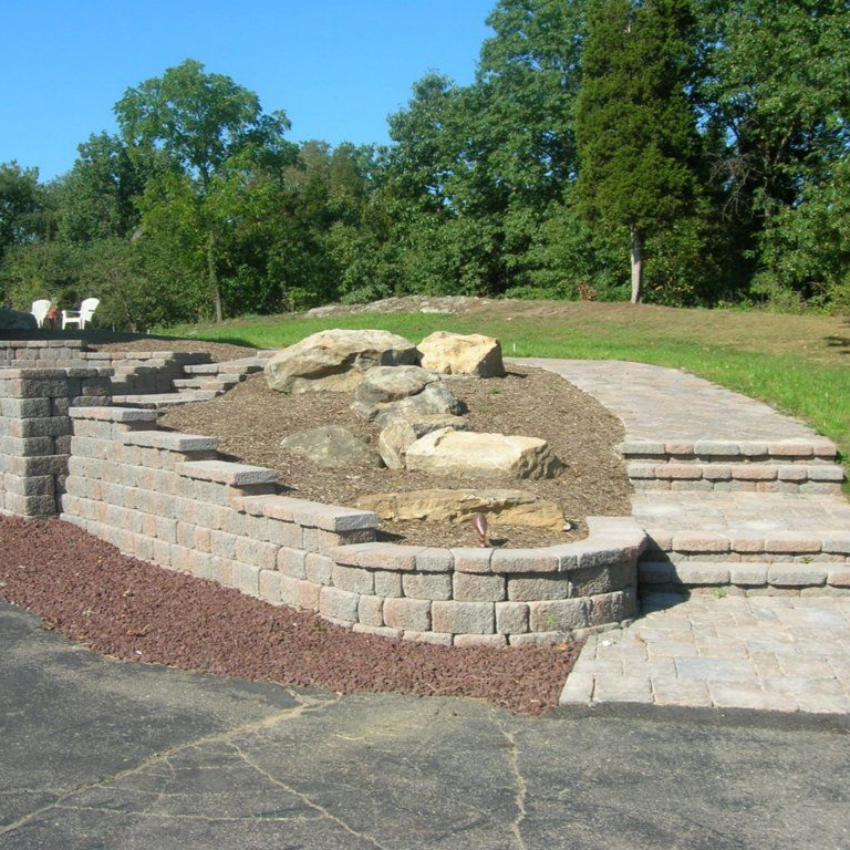 Curved stone garden planter with green foliage and purple flowers in a landscaped yard