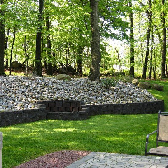 Curved stone garden path bordered by lush flowers and shrubs, leading to a small seating area under trees