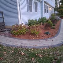 Stone walkway curving through a green suburban front yard beside a house in warm sunlight