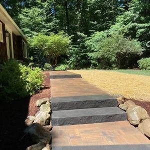 Patio garden with stone walkway, outdoor seating, and lush greenery under cloudy skies
