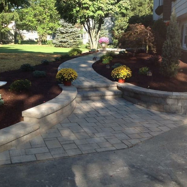 Stone garden path winding through lush hedges and colorful flowers under leafy trees