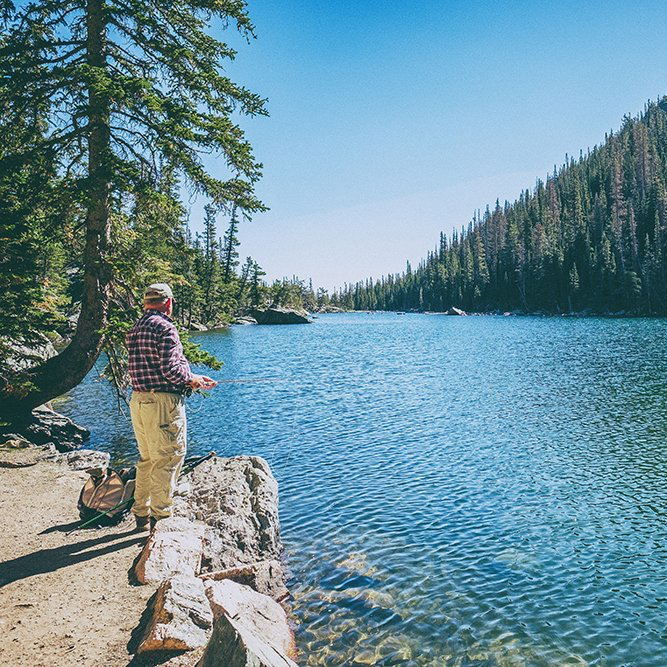 A man is standing on the shore of a lake fishing.