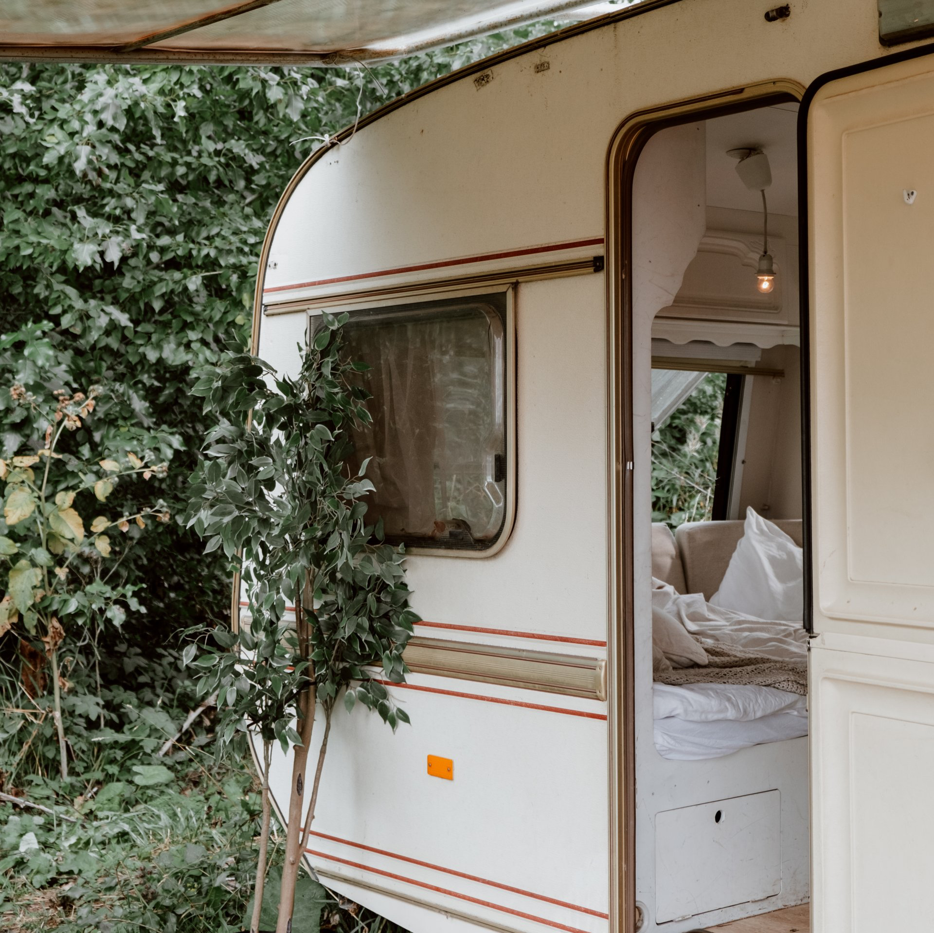 A white trailer with a bed inside of it is parked in the woods.