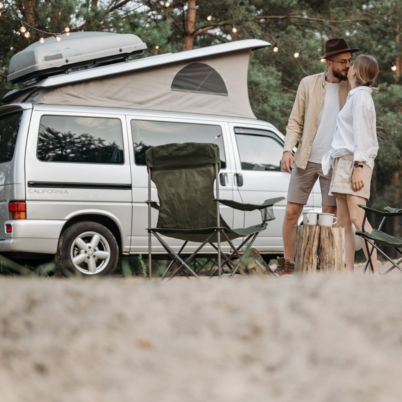 A man and woman are kissing in front of a camper van.