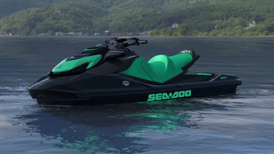 Black and green Sea-Doo jet ski floating on calm water with forested hills in the background