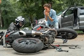 Woman stands near a fallen motorbike after a road crash, highlighting the urgent need for motorcycle accident lawyers.