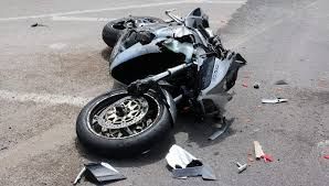 Damaged motorcycle lying on its side on a road, with debris scattered nearby.