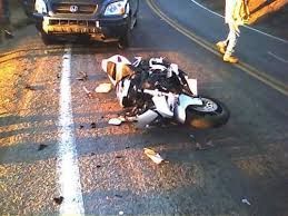 Motorcycle lying on its side after a crash on a wet road, with a car stopped nearby.