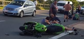 Overturned green motorcycle on roadside as bystanders and responders gather nearby