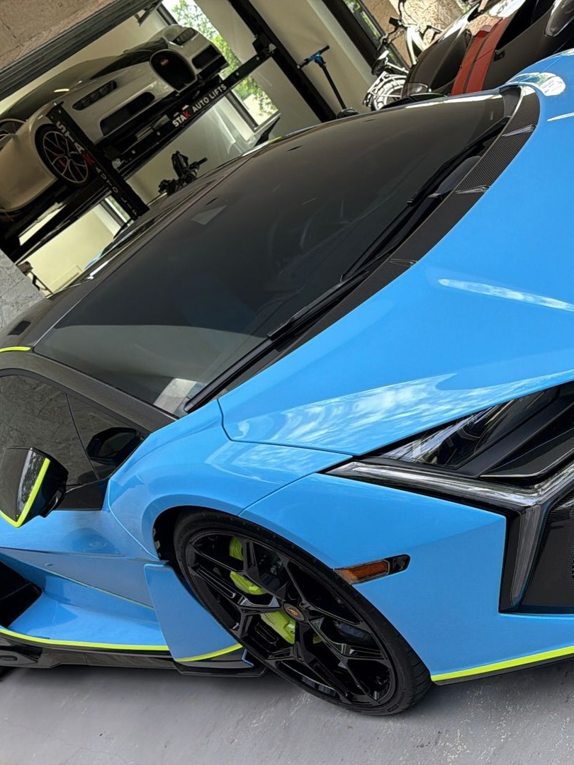Blue sports car with black roof and neon green accents parked indoors in a garage