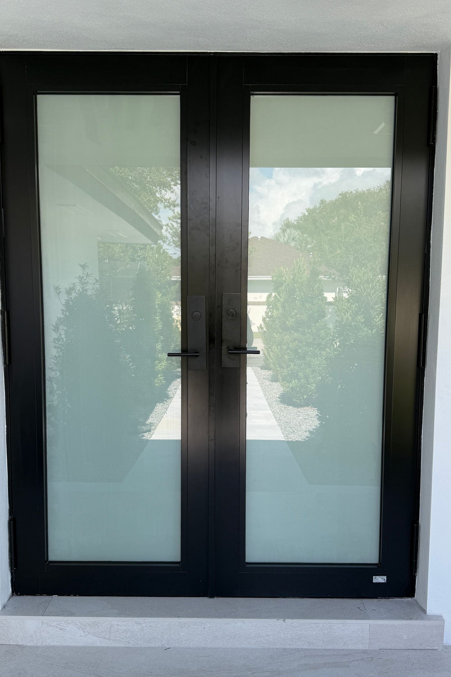 Black double glass doors with frosted side panels on a white exterior wall.