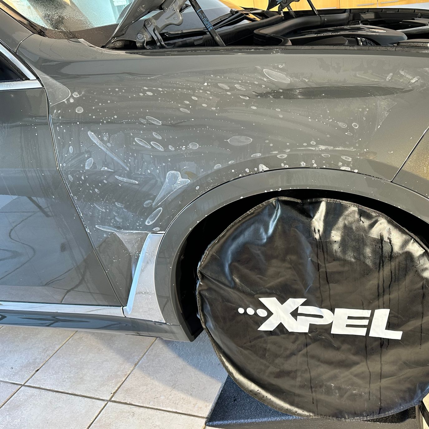 Car's front quarter panel with protective film. Black wheel cover with