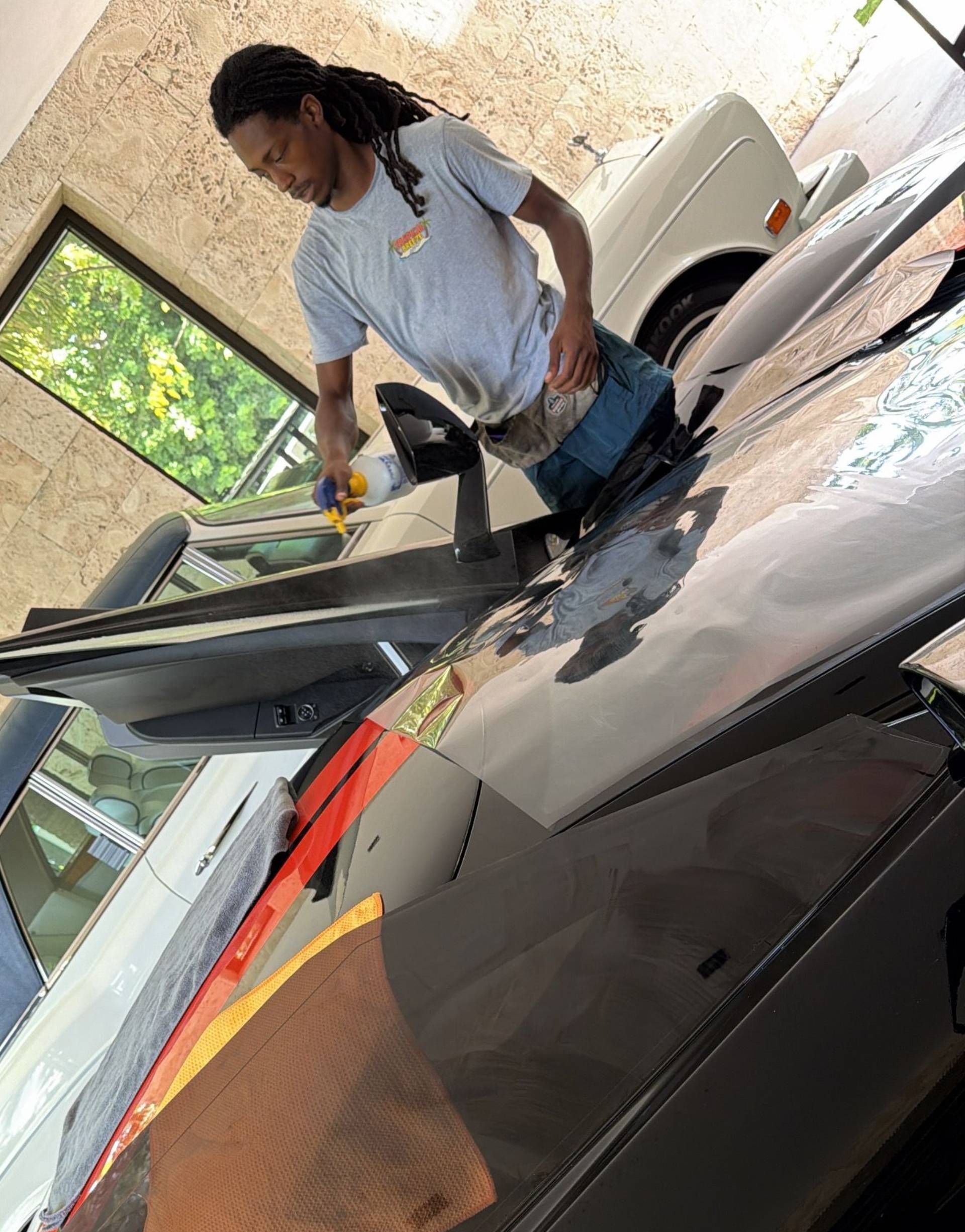 Person washing a black car in a garage, with a bright orange towel on the hood.
