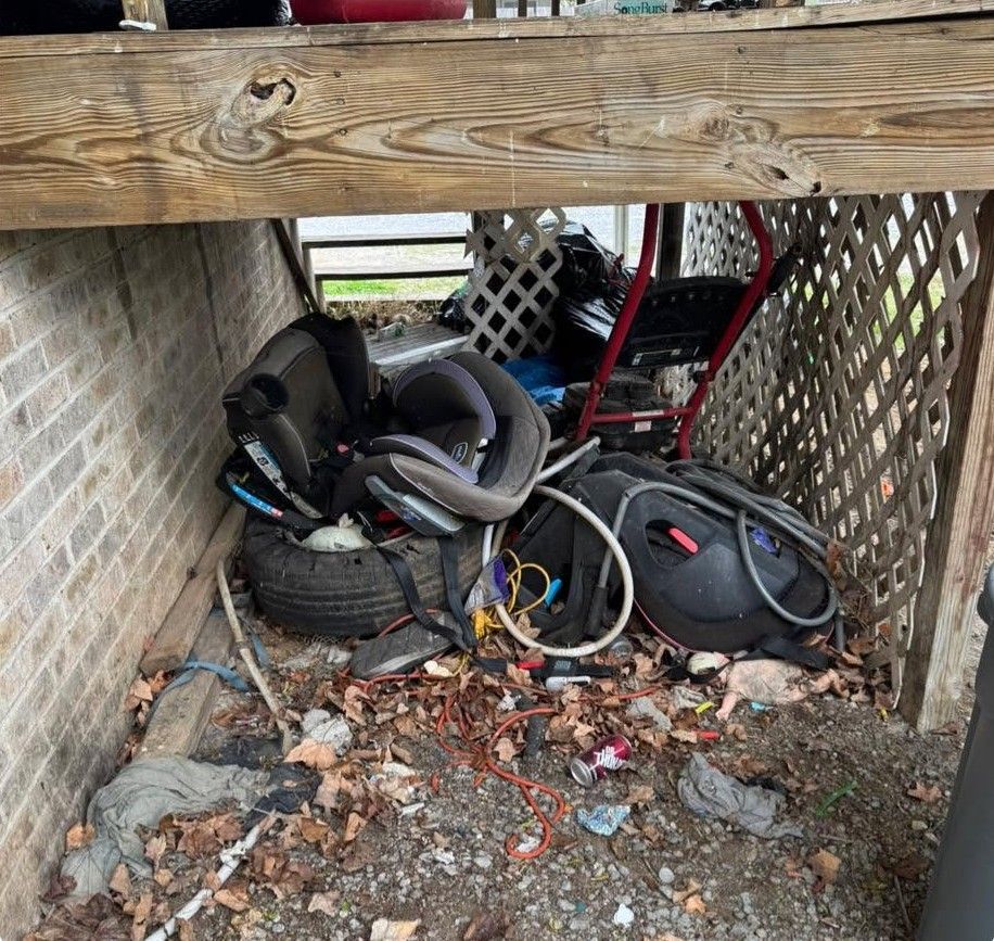 Piles of worn tires, hoses, and debris stored in a narrow covered outdoor space beneath a wooden beam.