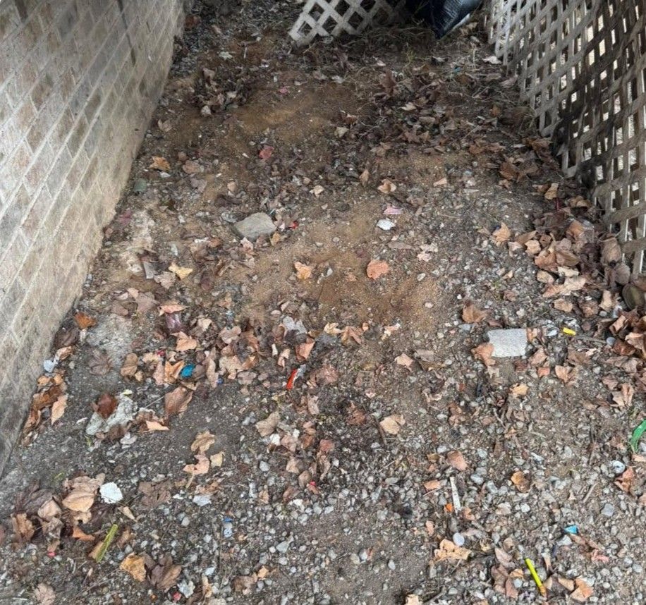 Narrow outdoor trench with dirt, gravel, and scattered debris between concrete walls