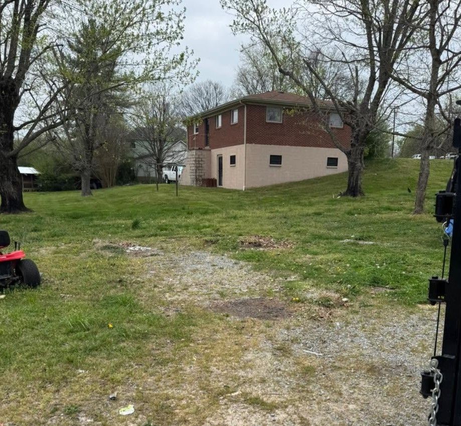 Two-story brick house with beige lower level in a grassy yard with trees and gravel driveway in front.