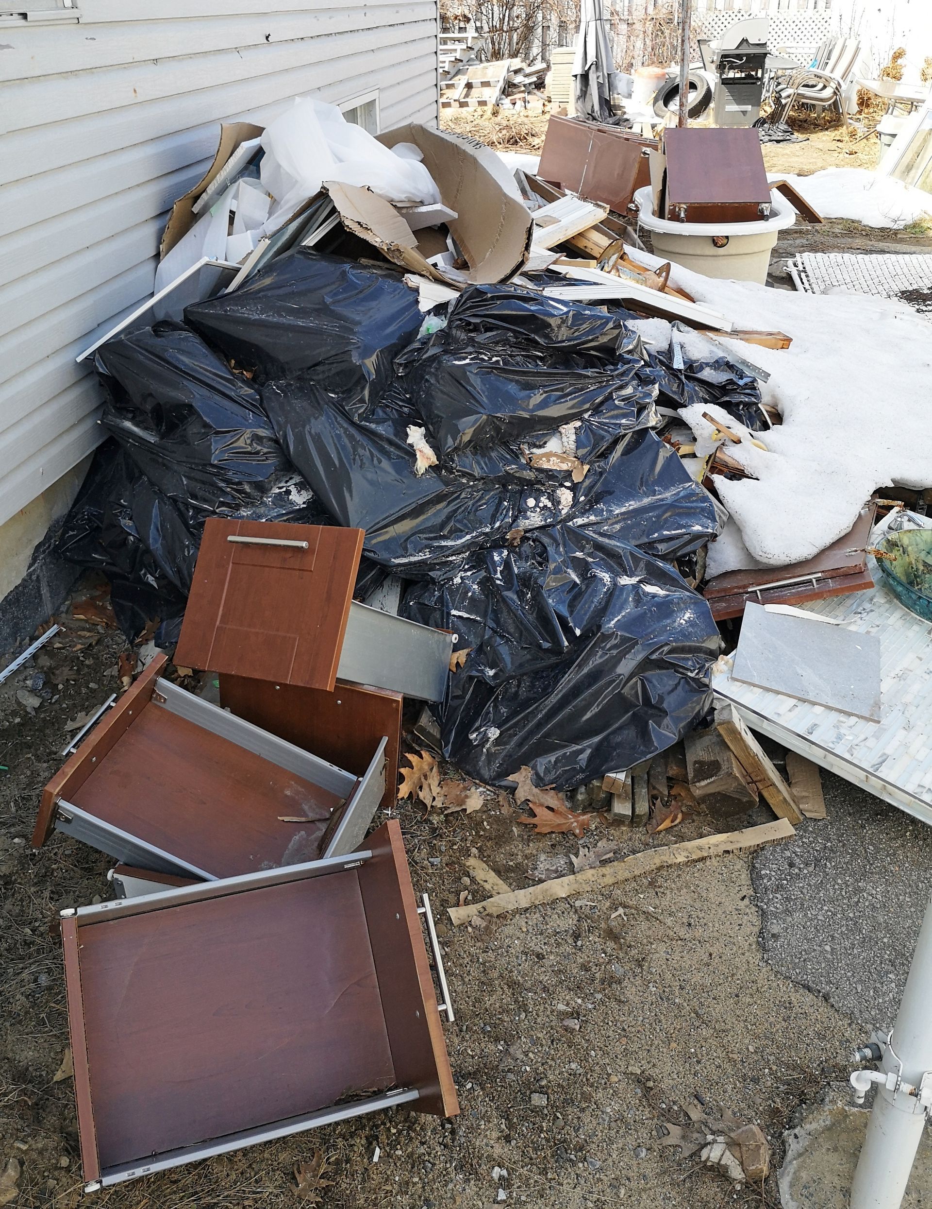 Storm-damaged yard cluttered with broken furniture, black tarp, and scattered debris beside a house