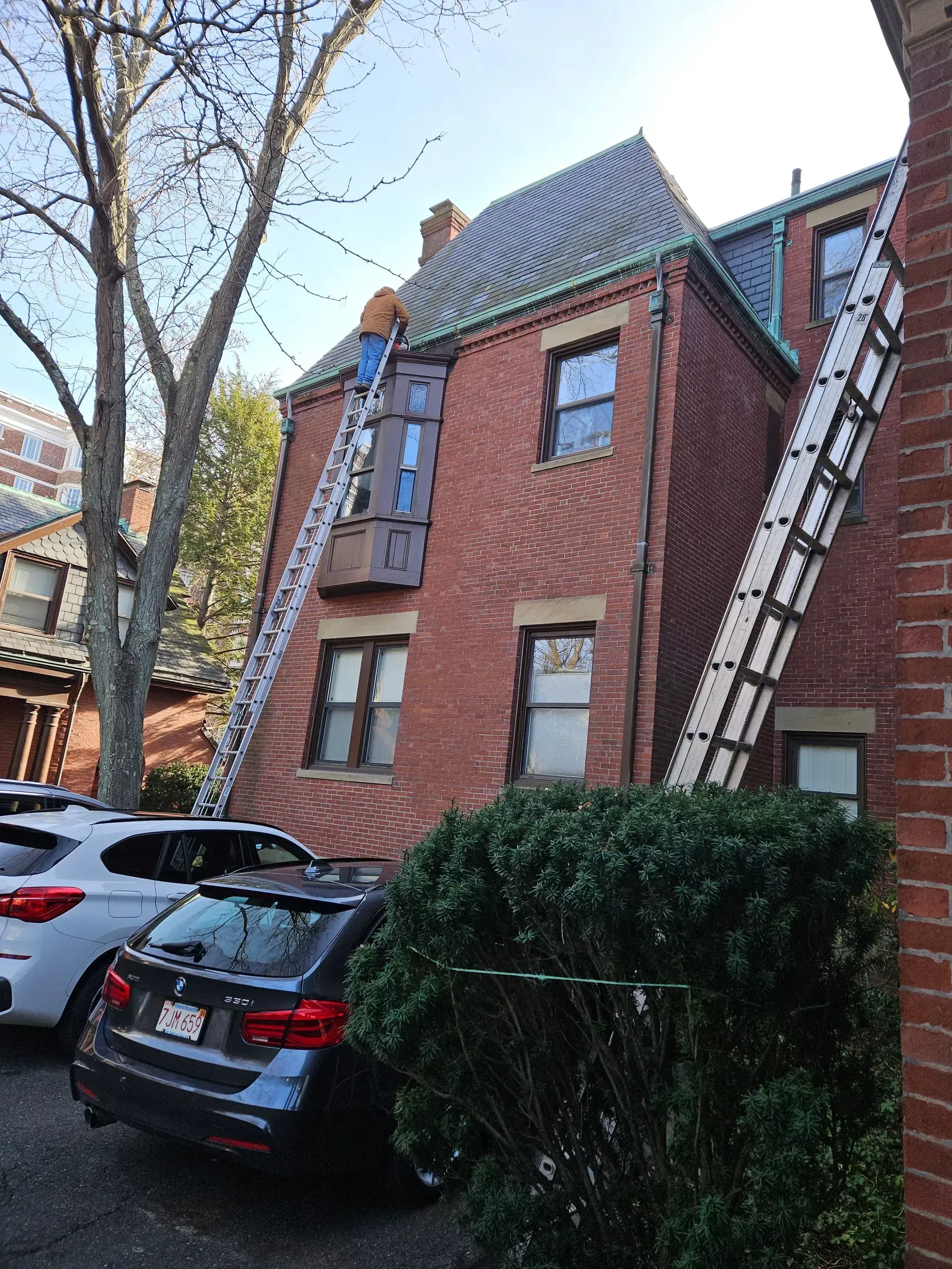 A man is standing on a ladder on the side of a brick building.